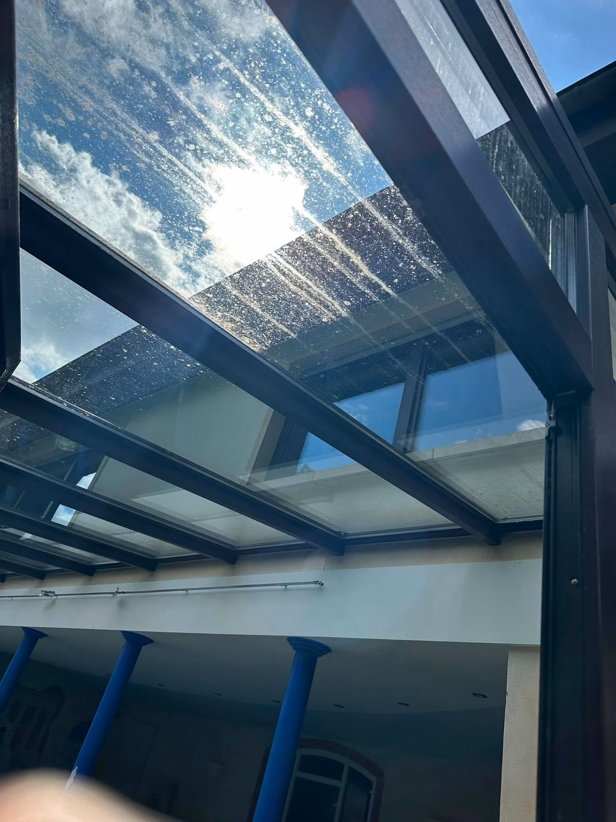 Verschmutztes Glasdach einer Terrassenüberdachung mit Wasserflecken vor der Reinigung